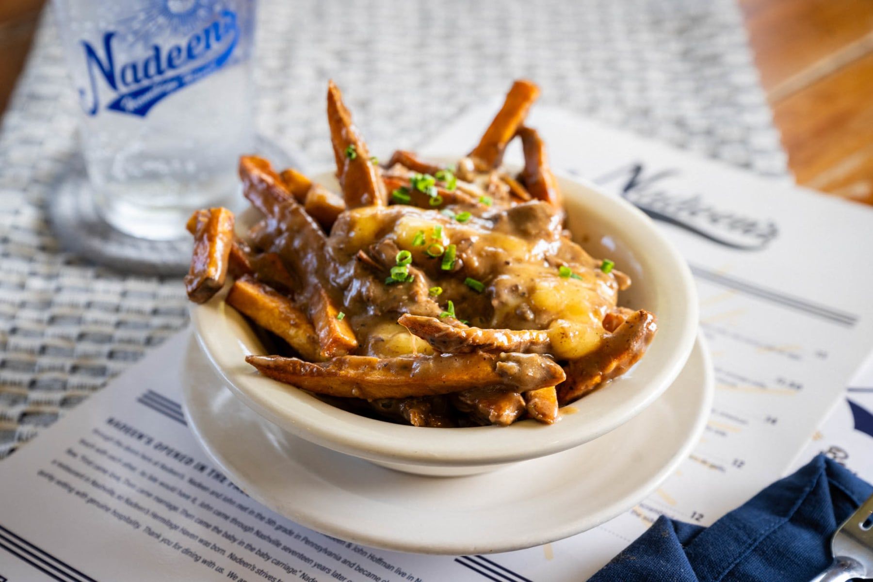 A hearty serving of fries topped with melted cheese, gravy, and chives—comfort food at its best. The cozy restaurant vibe and casual table setting invite guests to enjoy a laid-back dining experience.