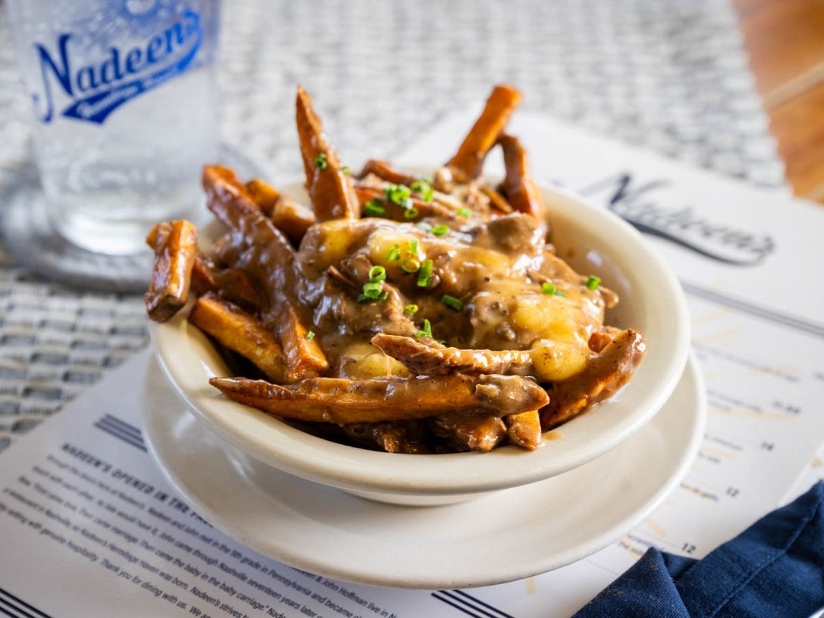 A hearty serving of fries topped with melted cheese, gravy, and chives—comfort food at its best. The cozy restaurant vibe and casual table setting invite guests to enjoy a laid-back dining experience.