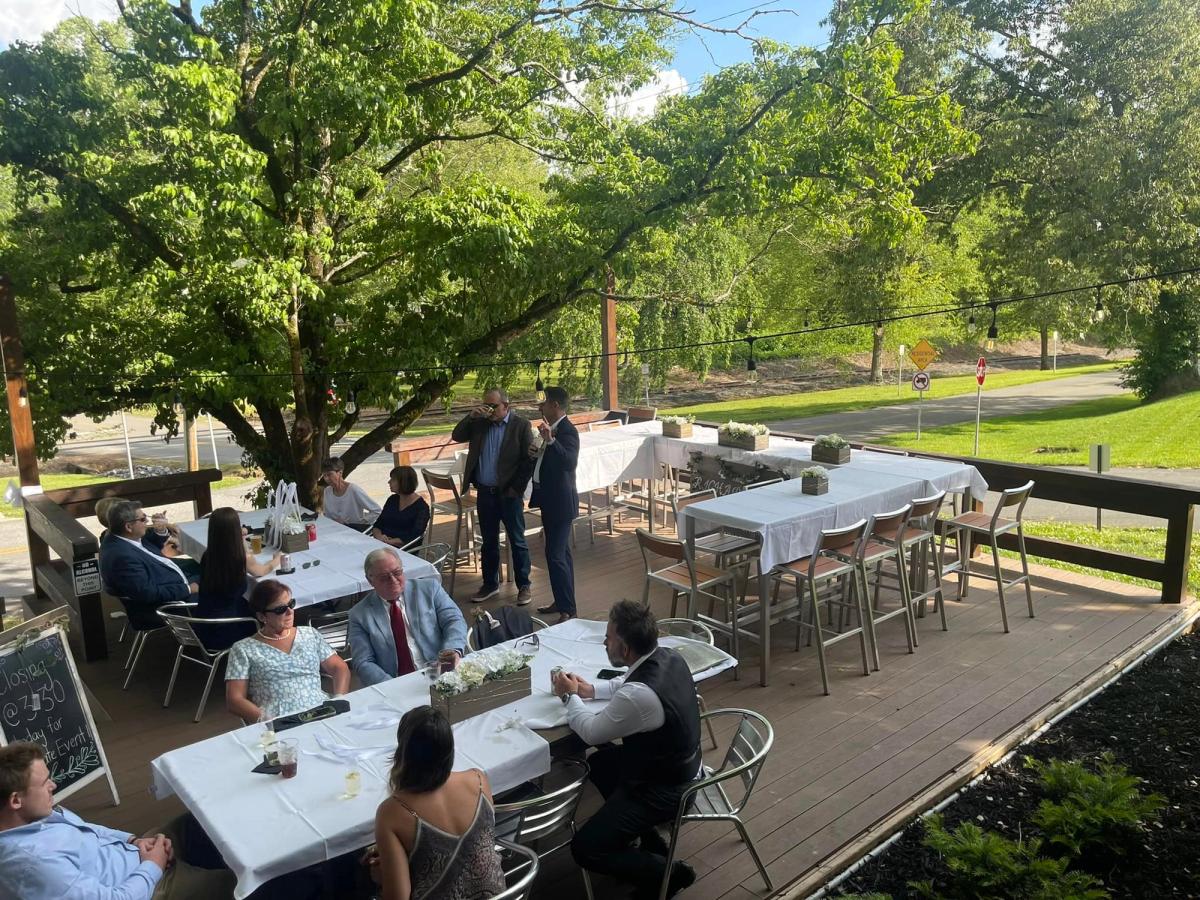 Guests relax on the outdoor deck at The Black Sheep Restaurant in Blue Ridge, surrounded by green trees and string lights. White table settings and open-air seating make it feel peaceful yet upscale. It’s a charming place for dinner in downtown Blue Ridge.