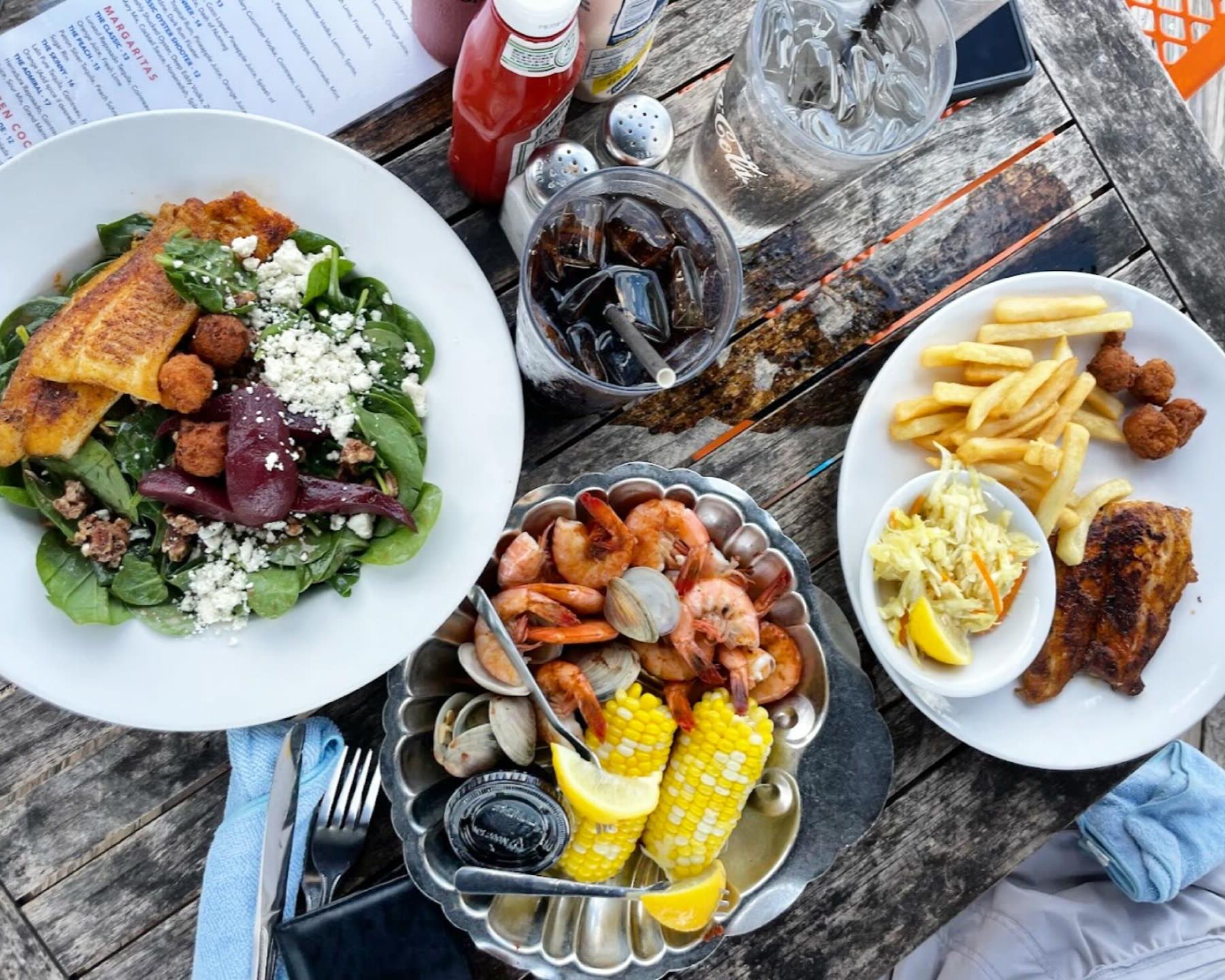 A seafood platter with shrimp, clams, corn on the cob, and fresh fish sits on a rustic table at Hudson’s Seafood House on the Docks. Cold drinks and waterfront views add to the relaxed coastal setting. It’s one of the top seafood restaurants on Hilton Head Island.