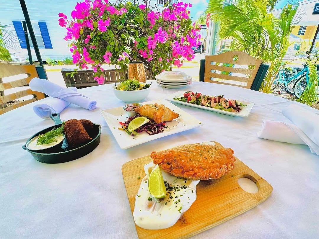 A colorful outdoor table at Santiago’s Bodega in Key West with empanadas, fresh salad, and small plates surrounded by vibrant flowers. A lively setting for tapas-style dining.