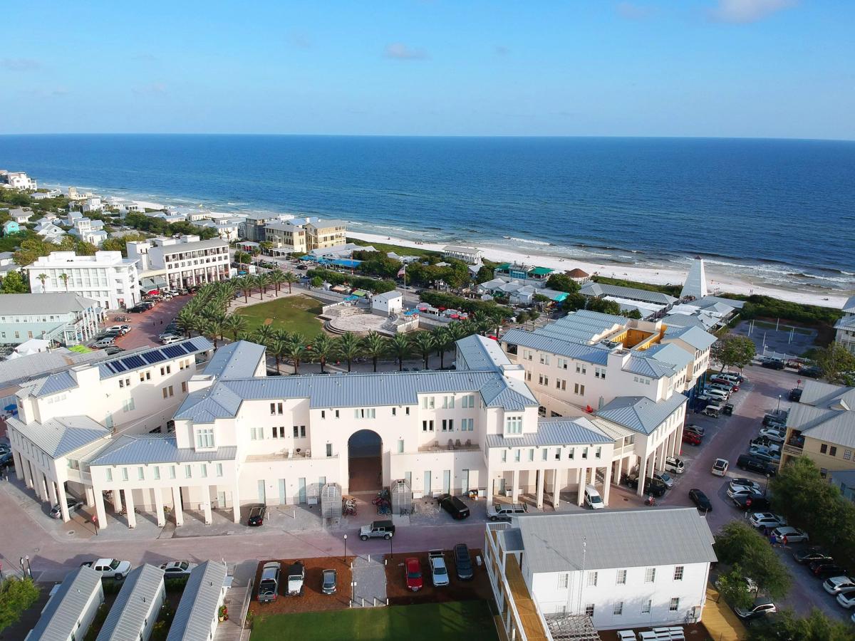 Aerial view of Seaside’s iconic amphitheater shows pastel buildings, palm trees, and a grassy lawn near the Gulf of Mexico. This lively town square hosts outdoor movies, music, and family-friendly events steps from the beach.