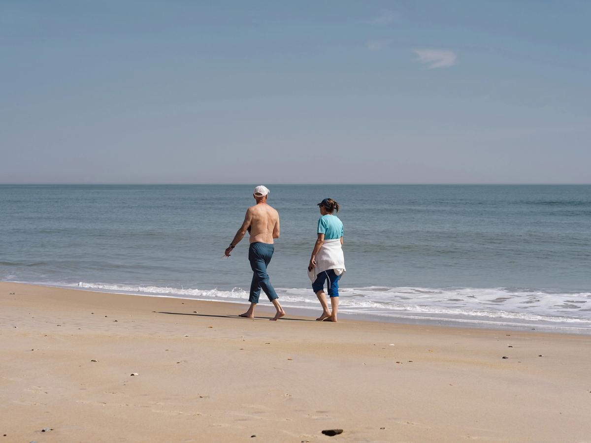 Older couple walking barefoot along the shoreline of a quiet beach in Chincoteague Island, Virginia, enjoying a peaceful coastal getaway.