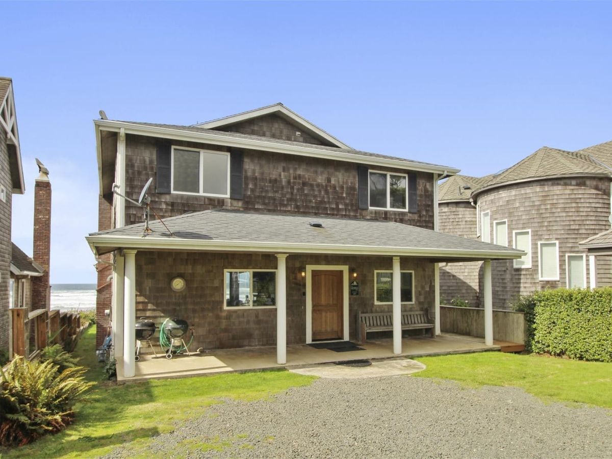 A cozy two-story beach house with shingle siding, white columns, and a welcoming front porch just steps from the ocean. Perfect for families, this charming coastal retreat offers comfort and easy beach access.
