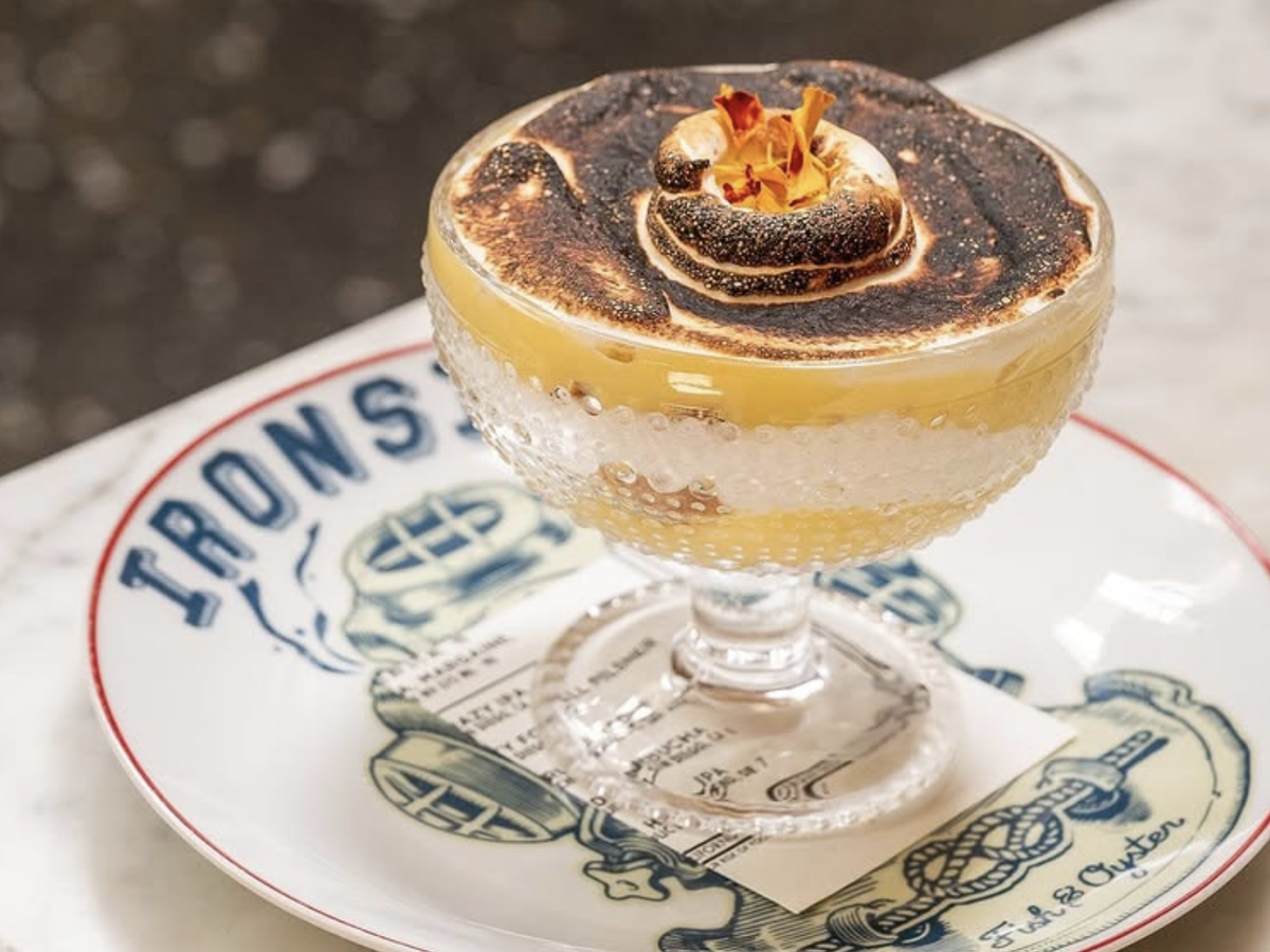 Elegant dessert in a glass coupe topped with toasted meringue and edible flowers, served on a decorative plate with nautical designs.