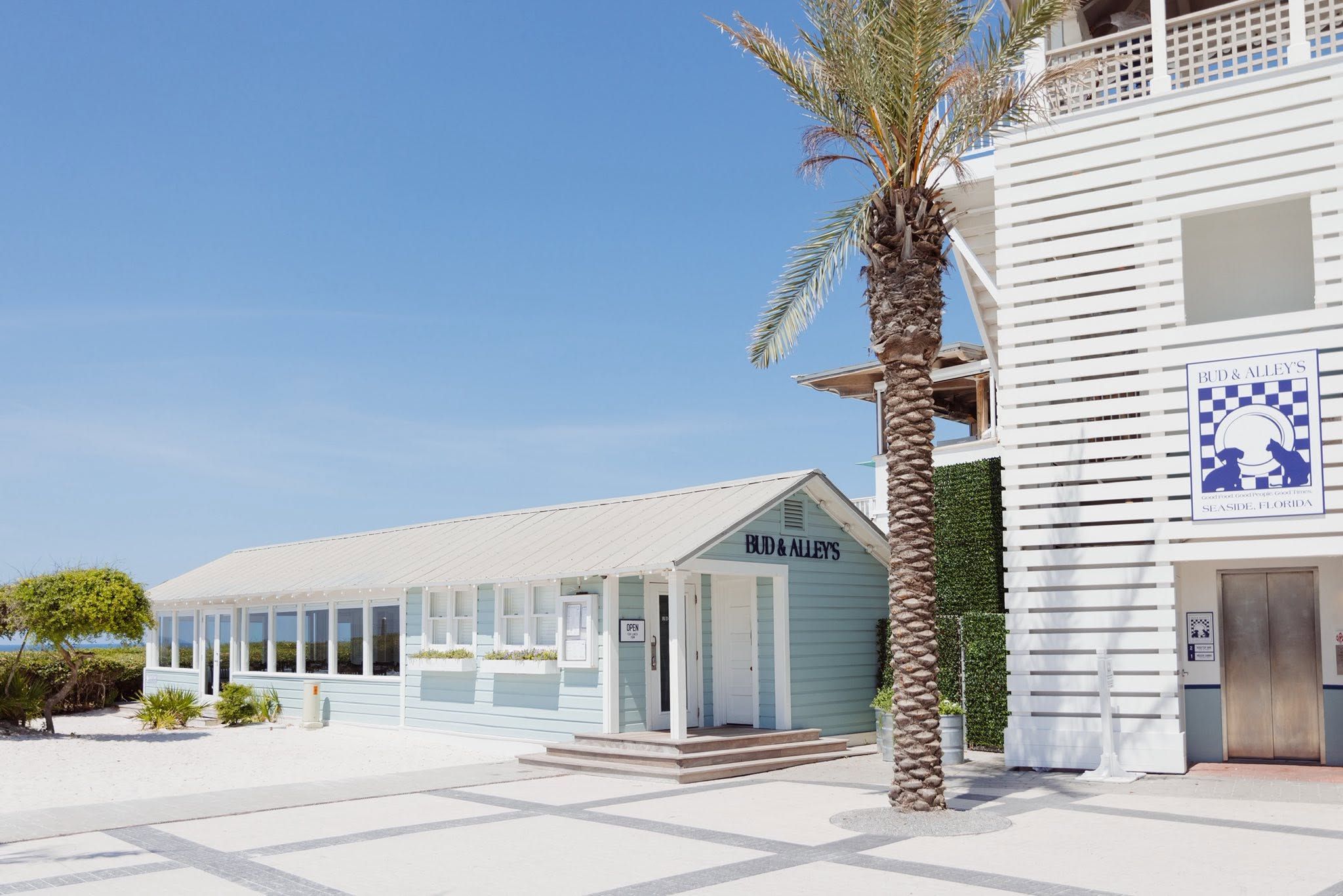 Bud & Alley's restaurant in Seaside, Florida along Scenic Highway 30A with coastal architecture, palm trees, and beach access on a sunny day.