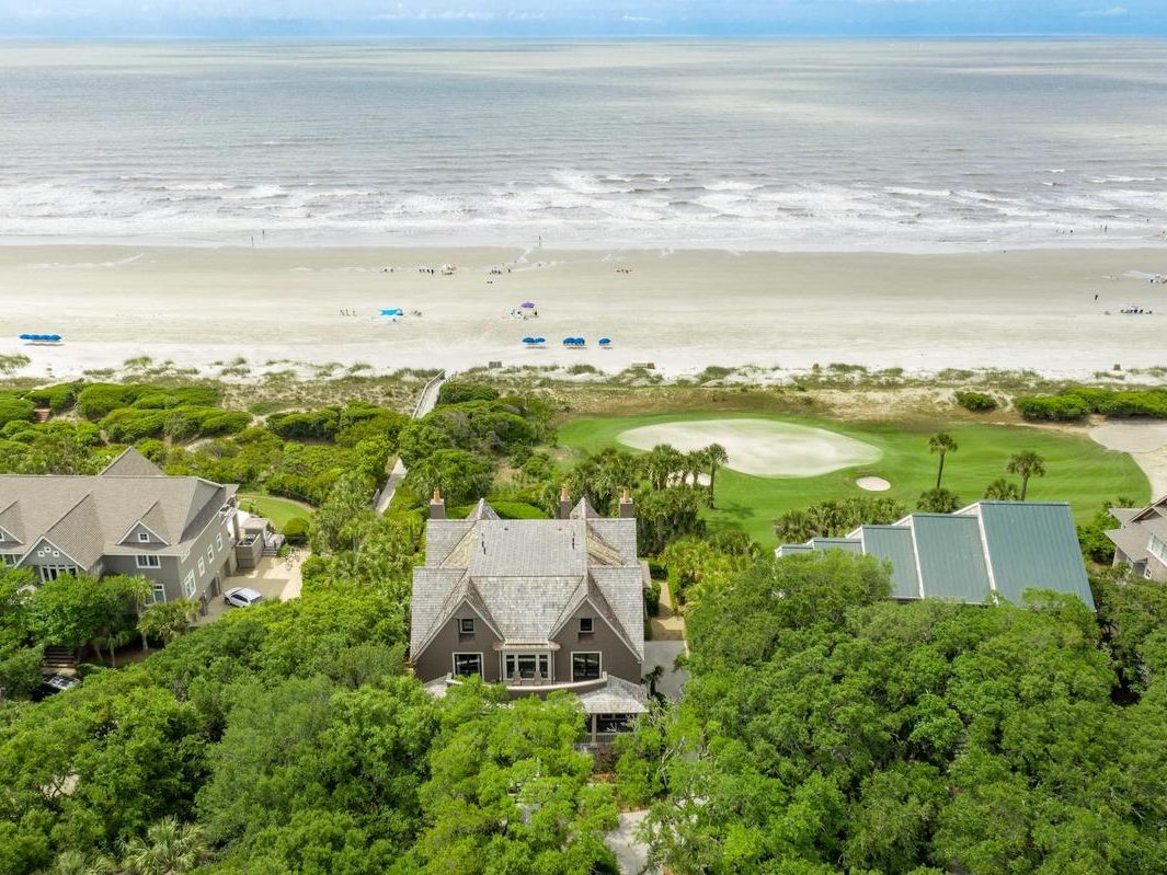 A beachfront golf course lined with luxury homes and lush greenery, steps from a quiet sandy shore. Perfect for vacationers who want ocean views and easy access to golf and beach fun.