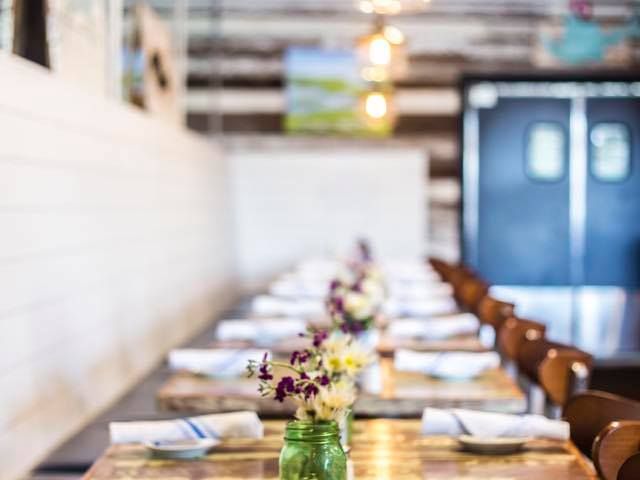 Inside Long Island Café, a long wooden table set with folded napkins and fresh flowers under warm pendant lights. A charming and relaxed space for gathering over local seafood and Lowcountry flavors.