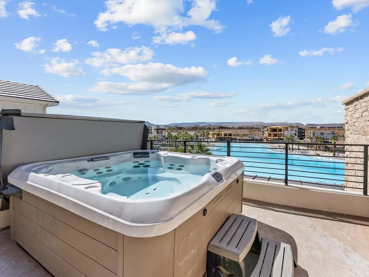 Rooftop hot tub with views overlooking a large resort pool and distant hills under a bright blue sky.