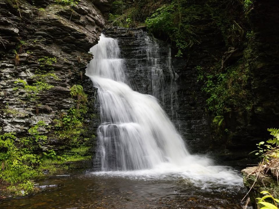 Bushkill Falls rushing down layered rock cliffs, surrounded by lush greenery in the Poconos.