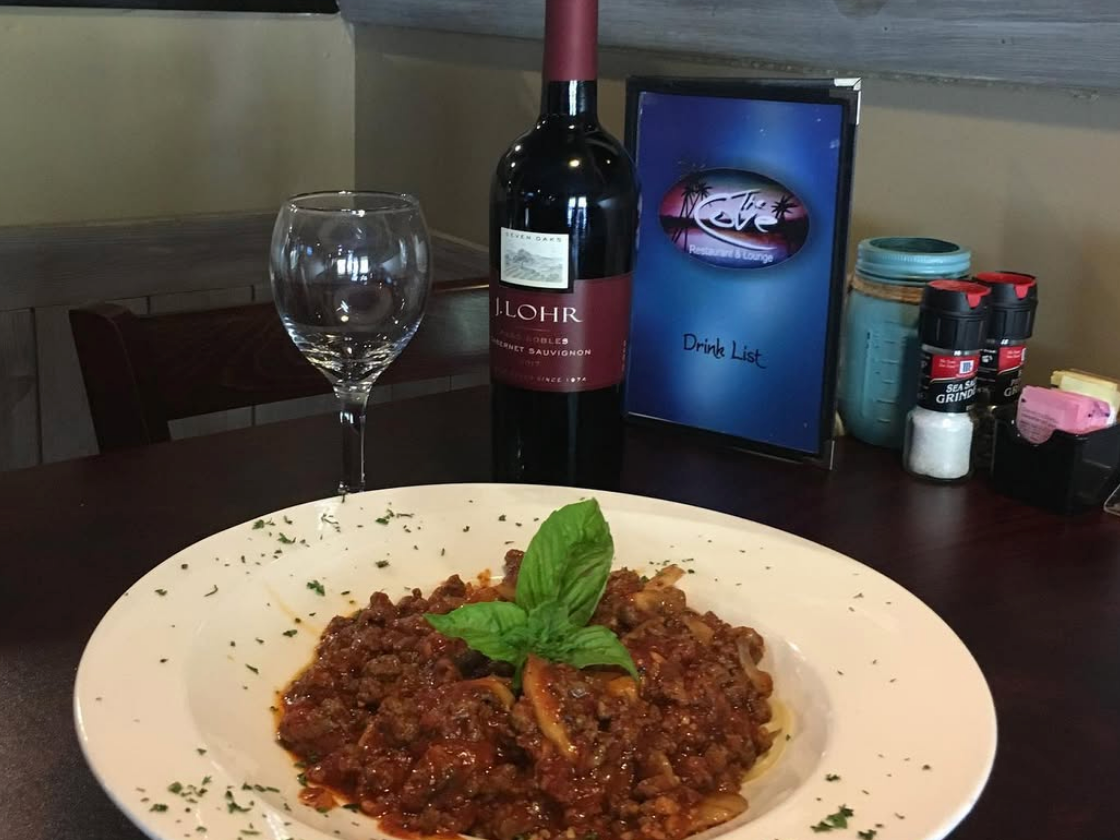 Bolognese pasta special with bay leaves on top in white bowl with wine bottle and wine glass