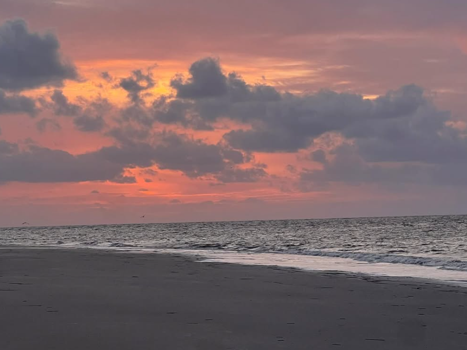 Pink. andorange sunset with clouds in the sky and beach with ocean waves gently on beach
