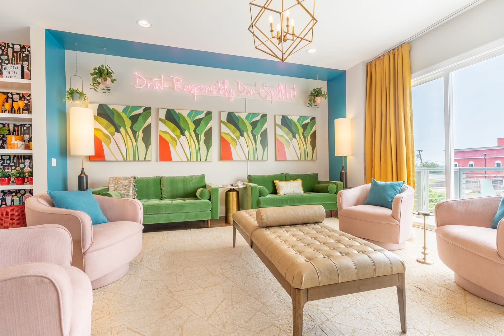 A stylish living room filled with color and natural light features green velvet sofas, blush pink chairs, and modern art on the walls. The elegant setting evokes the feel of a private, exclusive stay designed for comfort and fun.