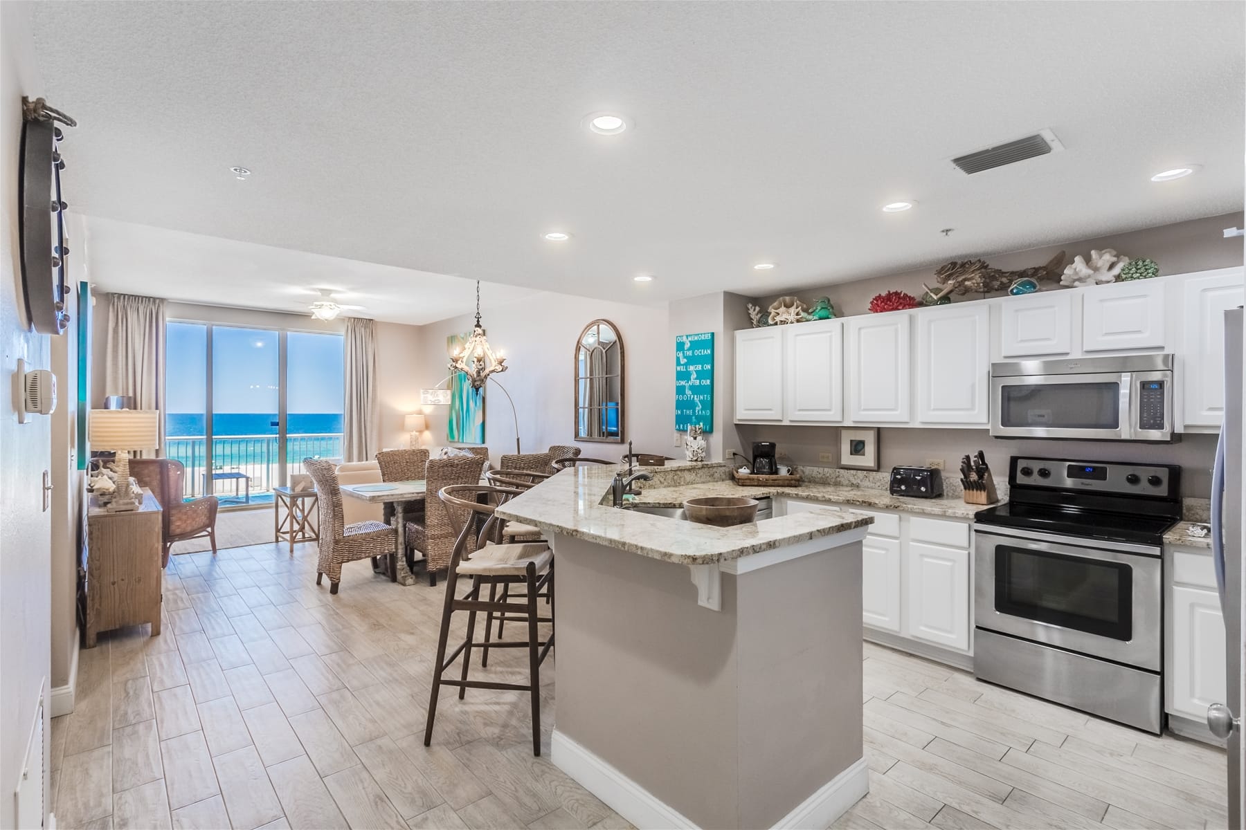 A cozy balcony setup with woven seating overlooks the turquoise Gulf waters. Bright pillows and a blue outdoor rug add color, creating a warm space for lounging by the sea.