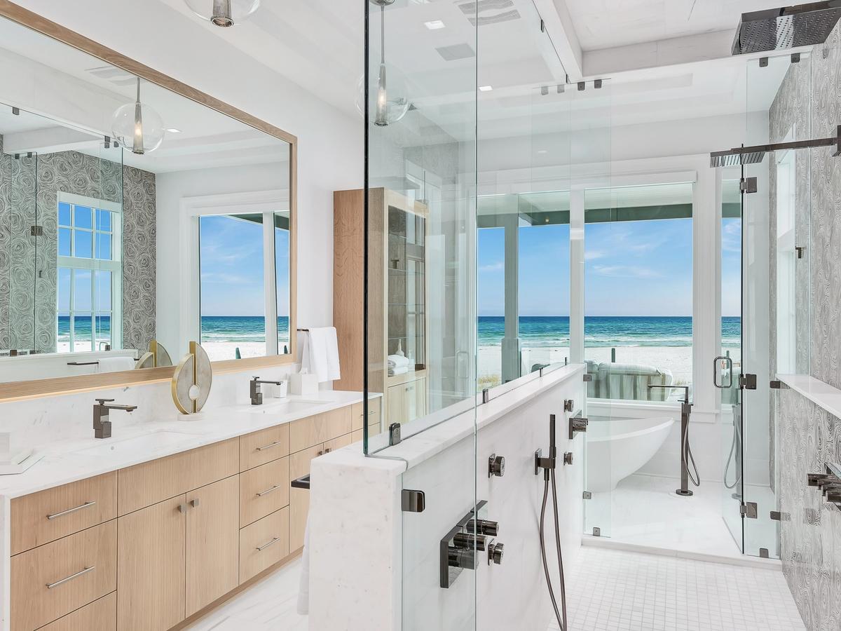 A luxurious beachfront bathroom with a spacious glass shower, dual rain showerheads, a modern freestanding tub, and large windows offering stunning ocean views.