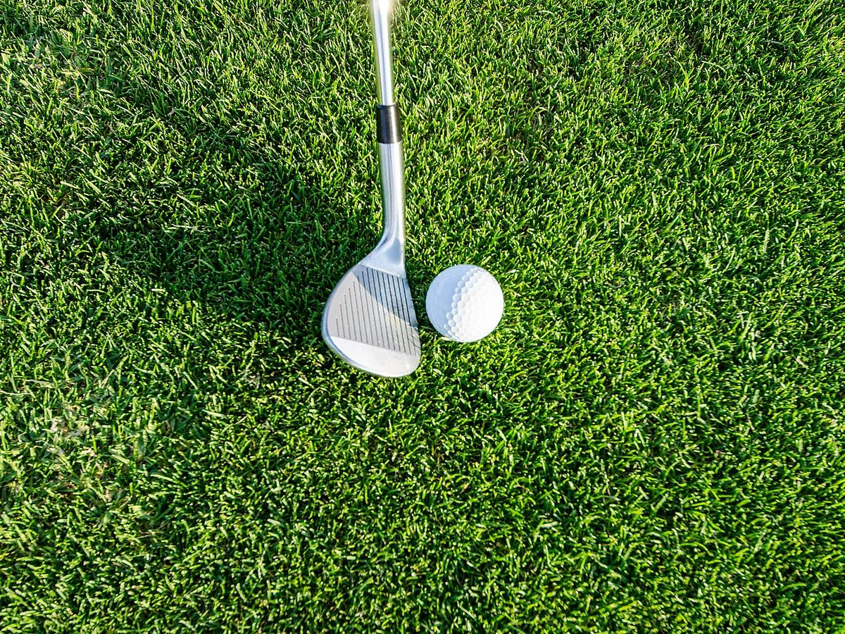 Close-up of a golf ball positioned next to an iron wedge on a well-manicured green grass surface, ready for a shot