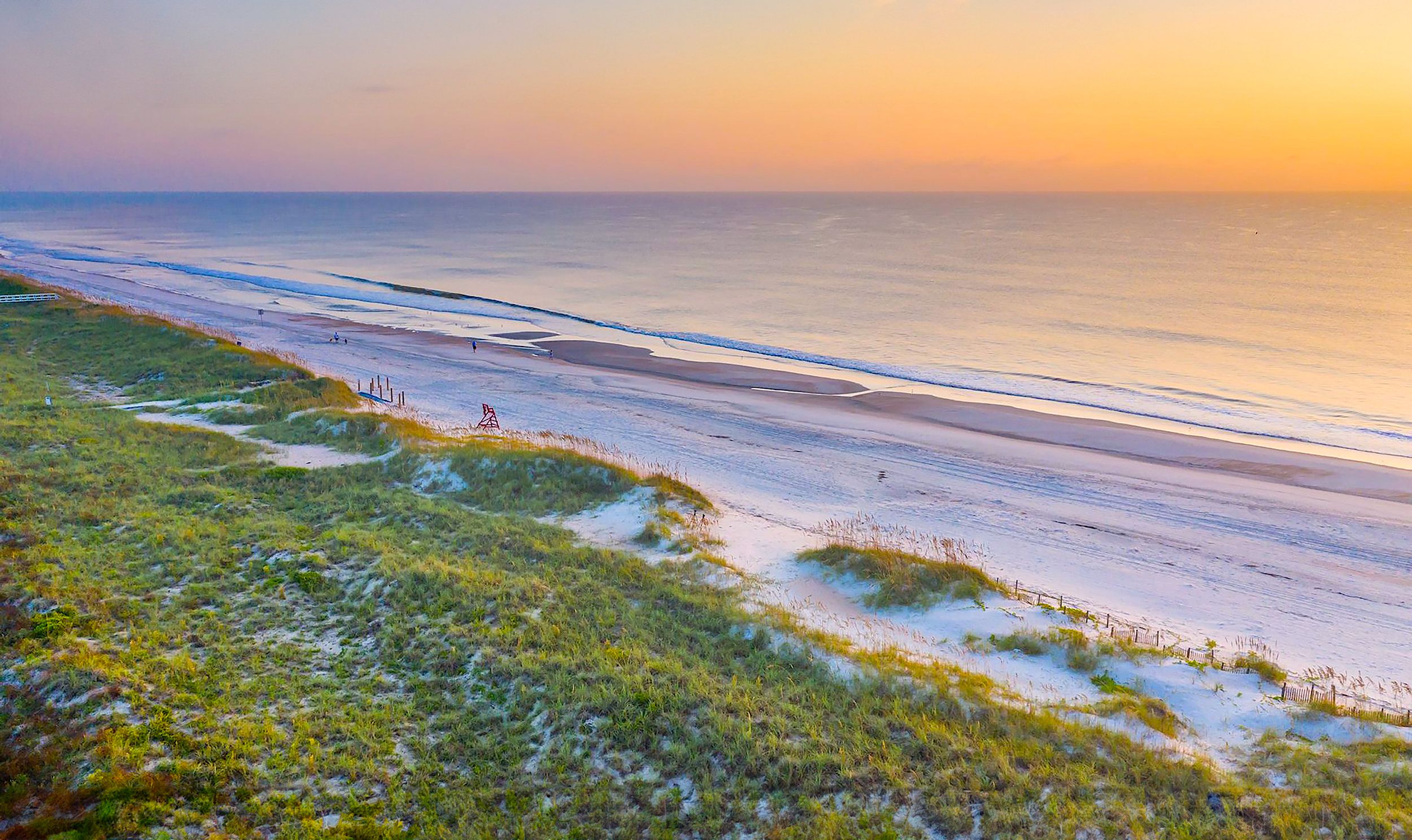 Sunset going down at beach with grassy land beside it