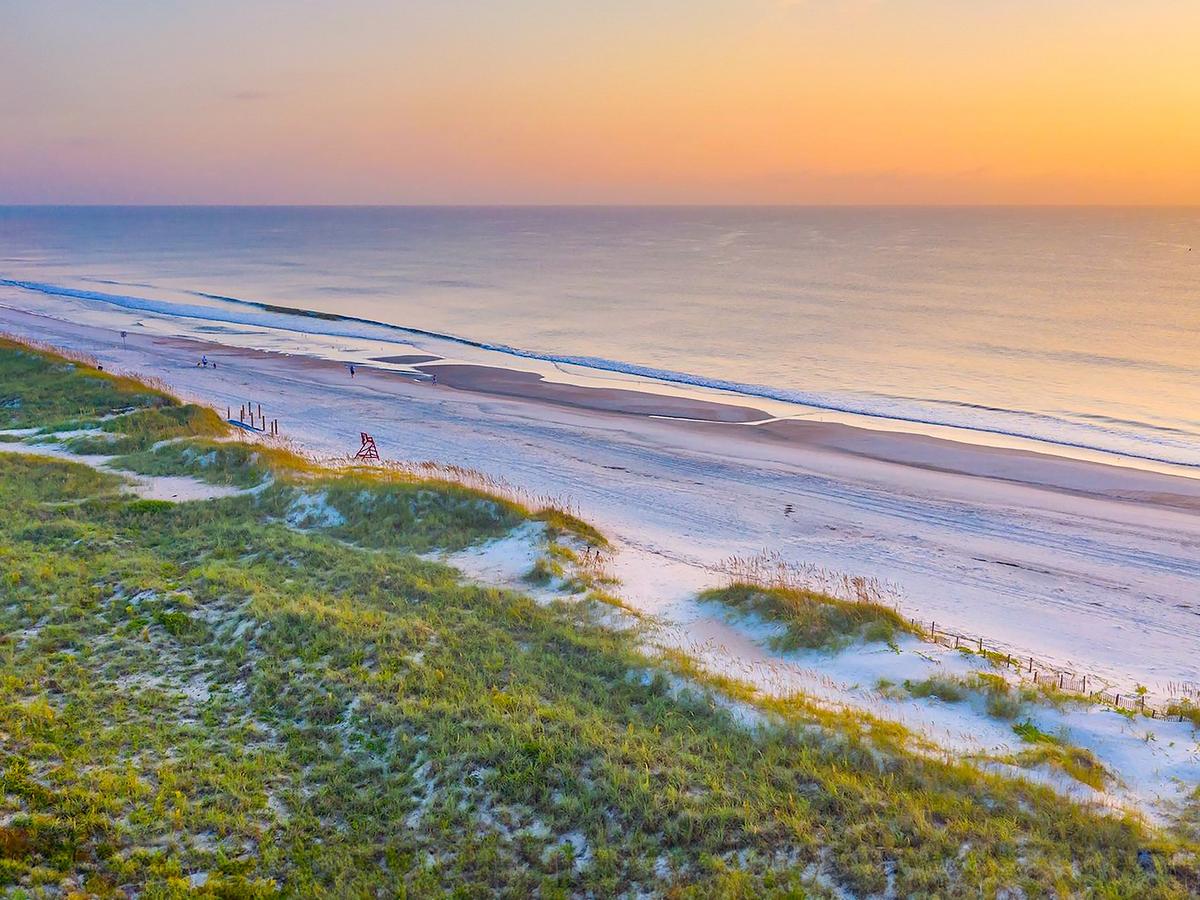 Sunset going down at beach with grassy land beside it