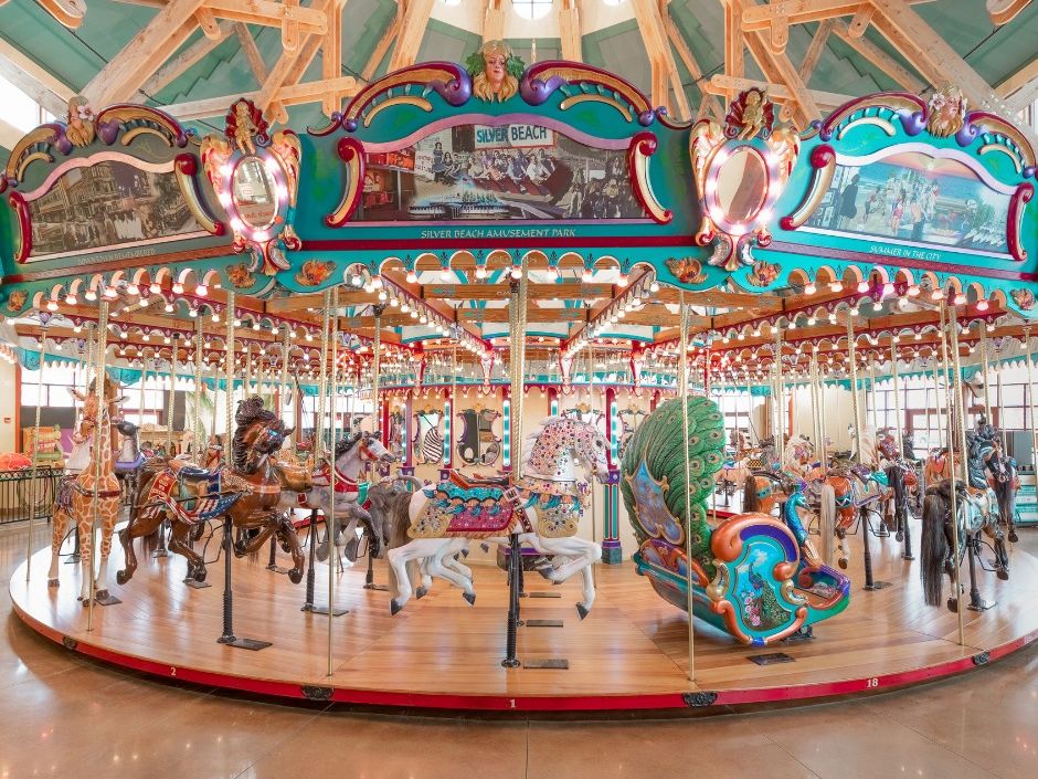 A vibrant and beautifully restored carousel filled with colorful hand-carved horses and whimsical decorations brings joy to visitors of all ages. The bright lights and classic details create a nostalgic, fun atmosphere inside the pavilion.