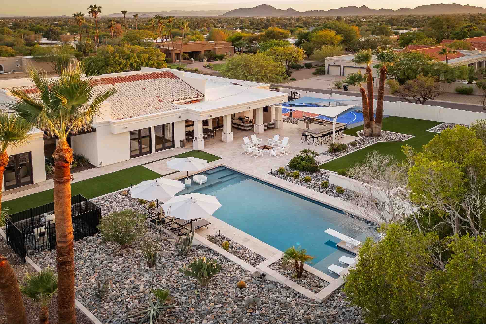 A luxury desert estate with a resort-style pool, expansive outdoor entertaining spaces, basketball court, and sweeping mountain views surrounded by lush landscaping.