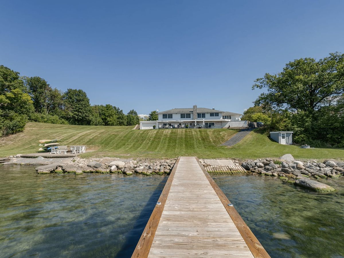 A tranquil Finger Lakes retreat with a private dock stretching over clear blue water. The open lawn and sunny skies make this home ideal for lakeside mornings and family gatherings.