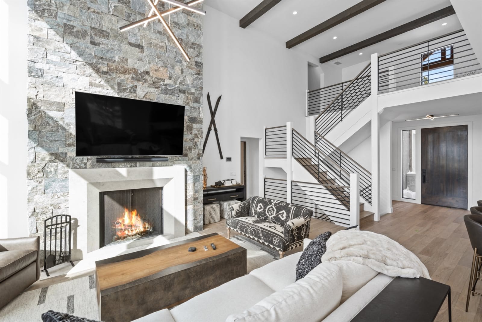A steaming hot tub sits on a covered wooden deck beside a stone cabin wall, with snowy trees and rustic wooden chairs in the background.