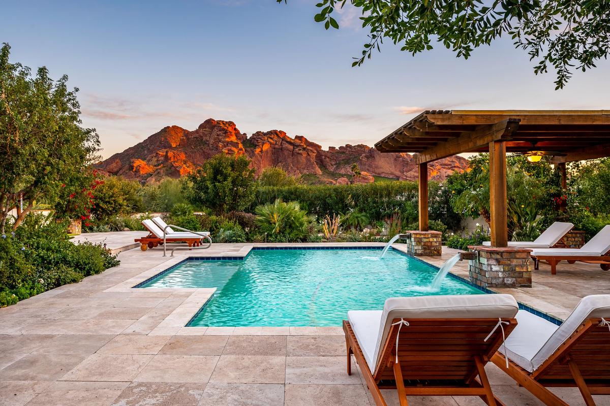 A private desert oasis with a sparkling pool and mountain views glowing in the evening light. Surrounded by palm trees and desert blooms, this Scottsdale retreat blends luxury and nature.