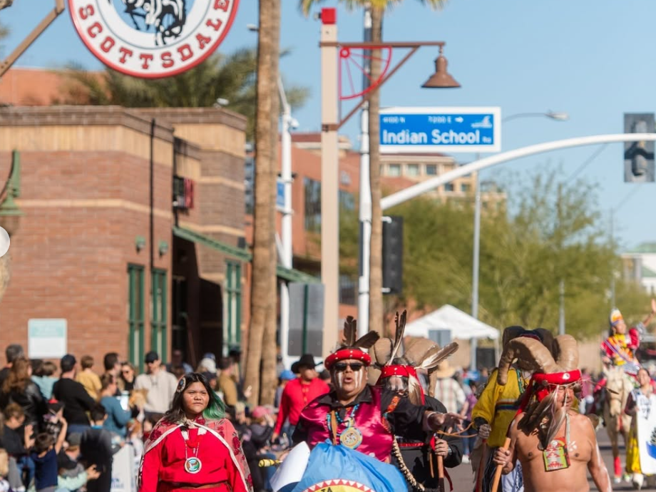 People walking in a parade with an old town scottsdale sign hanging above them
