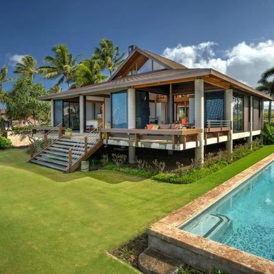 Home with open walls for indoor-outdoor living, overlooking a spacious lawn and a private pool.