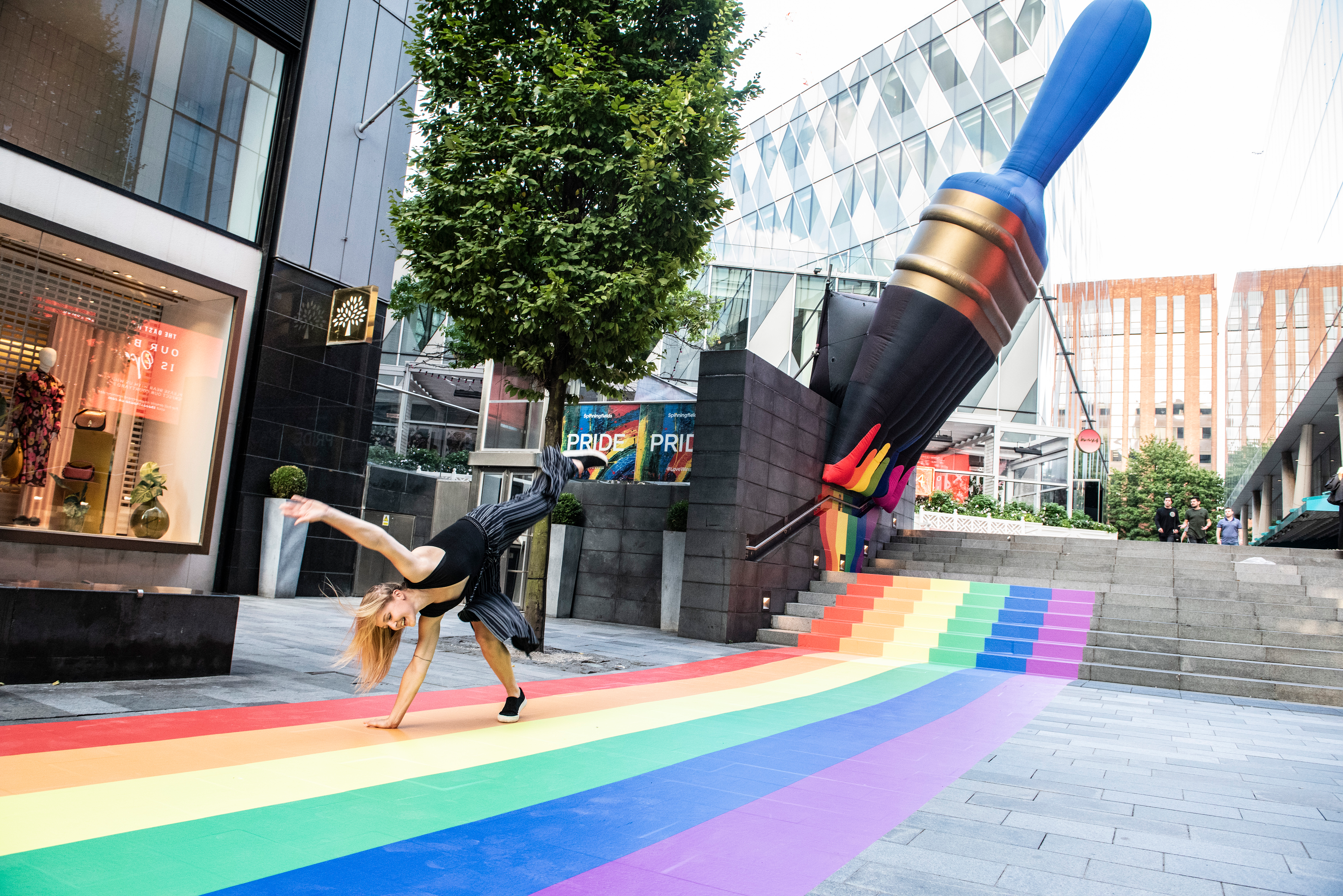 A girl cartwheeling down The Avenue in Spinningfields, over a Pride mural depicting a paint