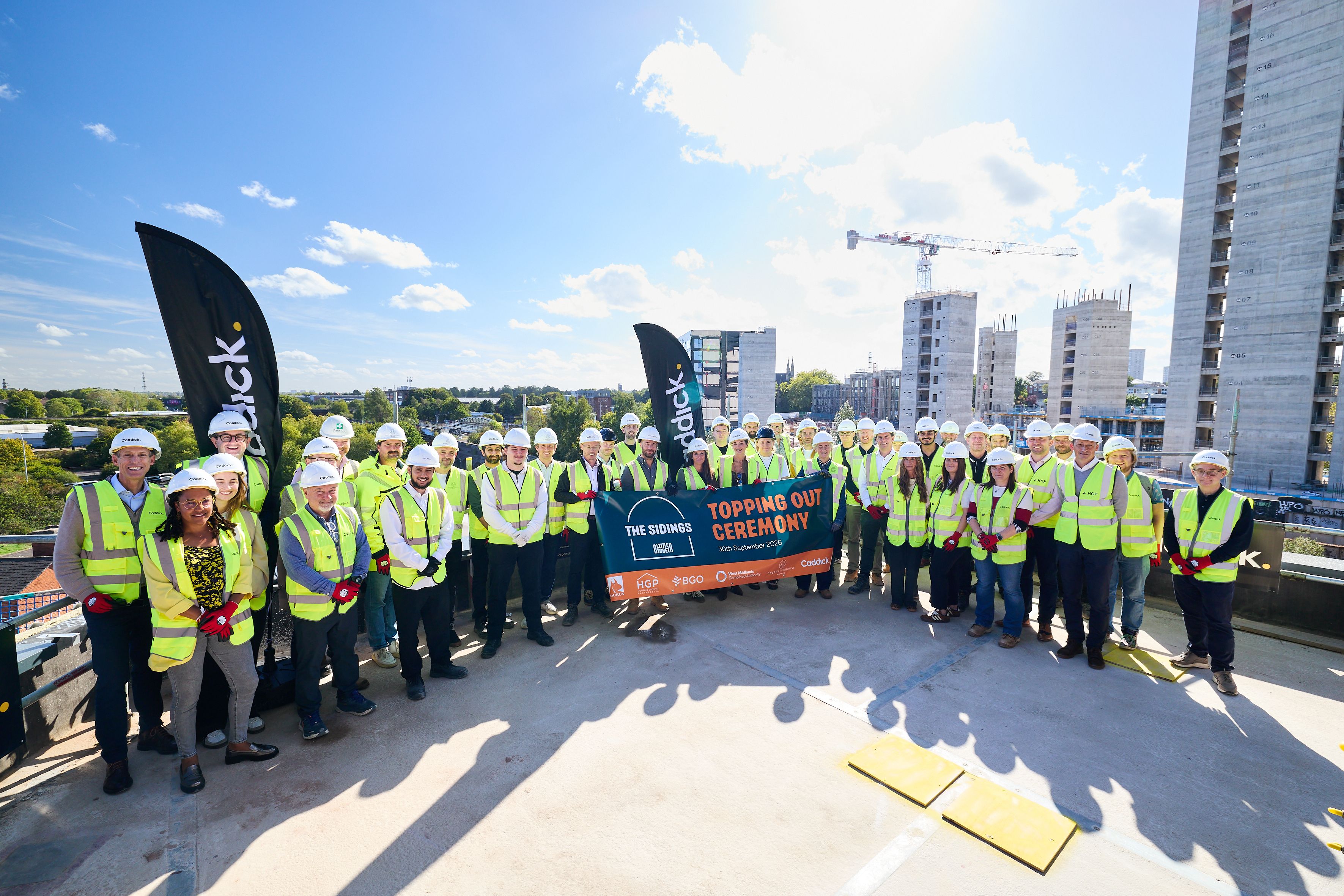 A large group of people involved with Little Digbeth's The Sidings stand with a banner at the top of the building