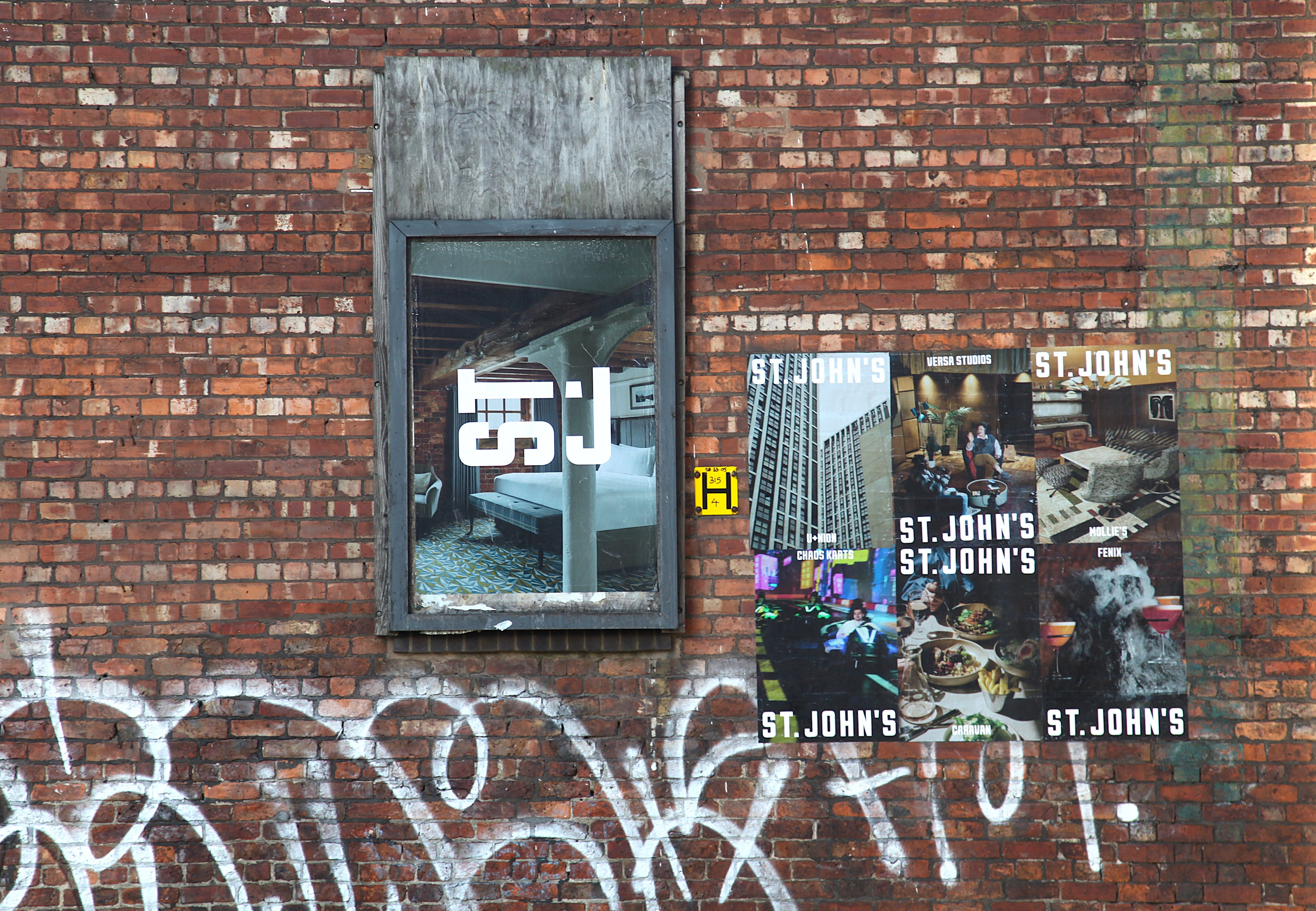 Flyposters of St. John's branding on a graffitied brick wall