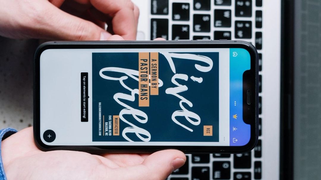 Phone held sideways over a laptop, showing a “Live free” sermon poster open in Canva’s mobile editor.