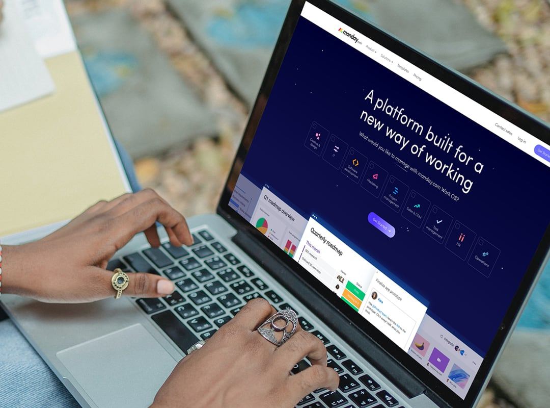 Laptop showing the monday.com homepage, “A platform built for a new way of working”, as someone types.