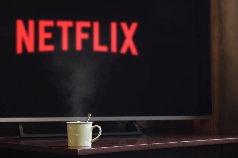 TV screen showing the Netflix logo, with a steaming mug on the stand in front of it.