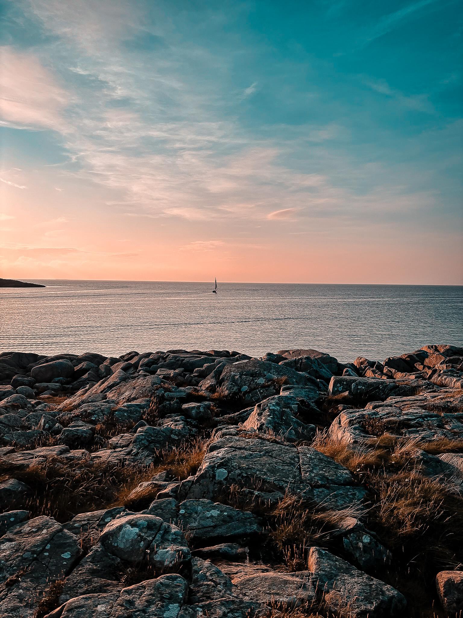 Sonnenuntergang an der Felsküste mit Blick auf ein Segelboot