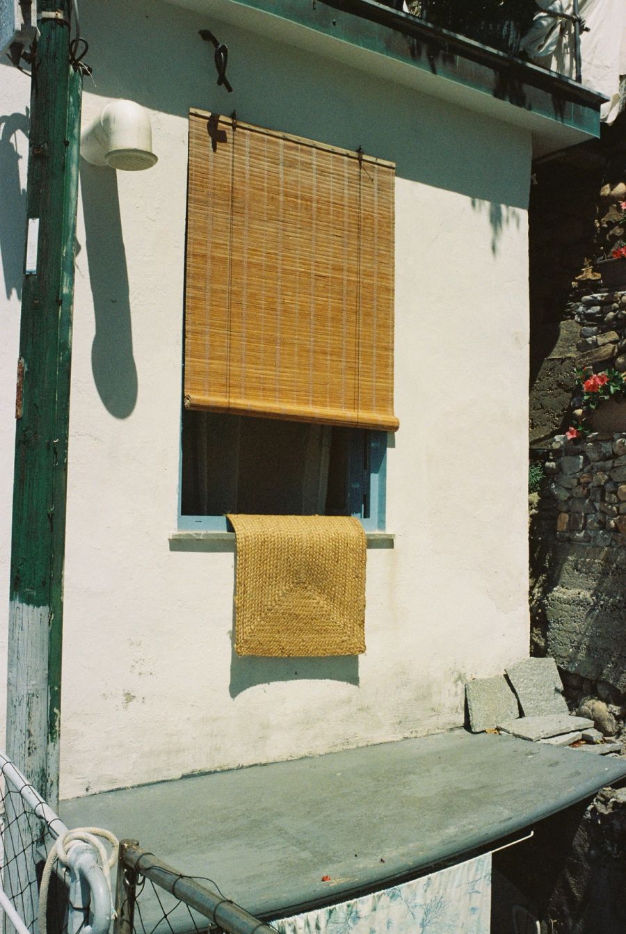 Bamboo blind and woven mat drying on a whitewashed seaside house, Italy. Film photograph by Nicolò Pudel