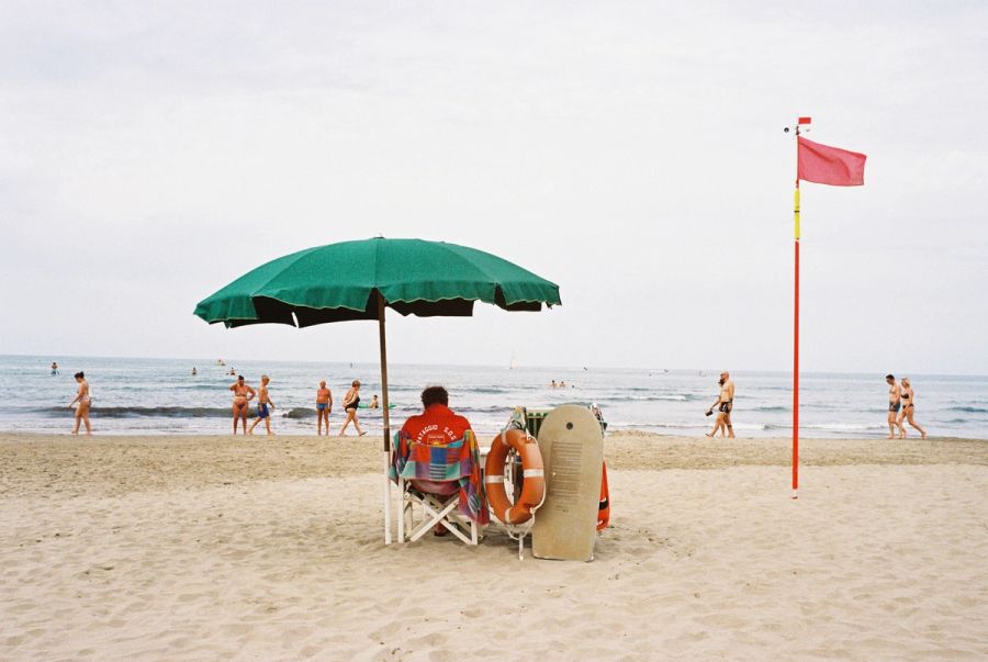Lifeguard under a green umbrella beside a red flag, Italian beach. Film photograph by Nicolò Pudel