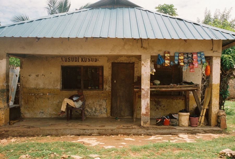 Man resting on the veranda of the Kusudi Kusudi shop, Msambweni, Kenya. Film photograph by Nicolò Pudel