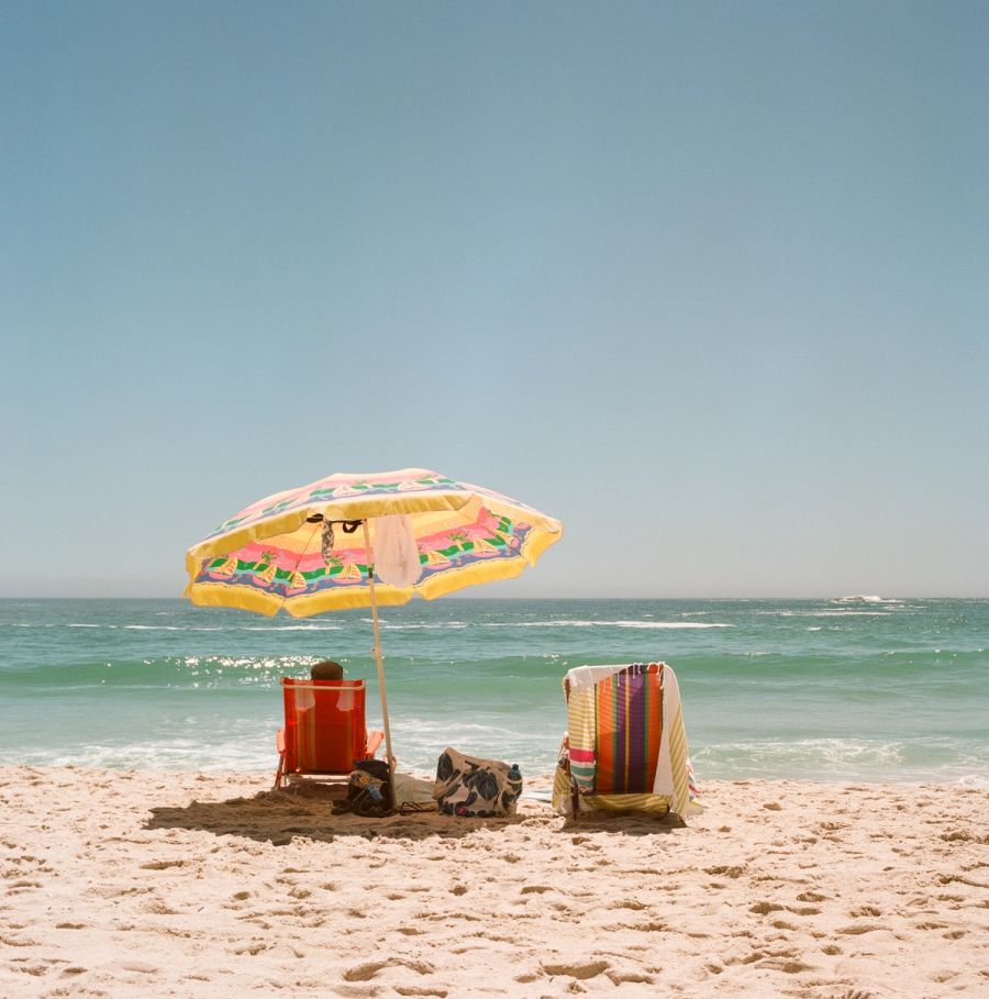 Bright striped umbrella and deck chairs facing the sea, Cape Town. Film photograph by Nicolò Pudel