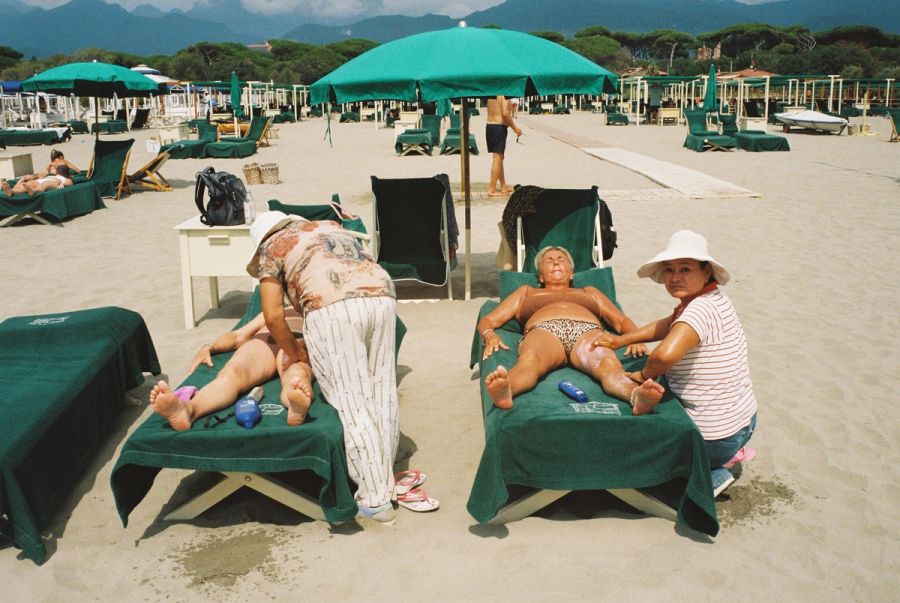 Bathers on green loungers under matching umbrellas at an Italian lido. Film photograph by Nicolò Pudel