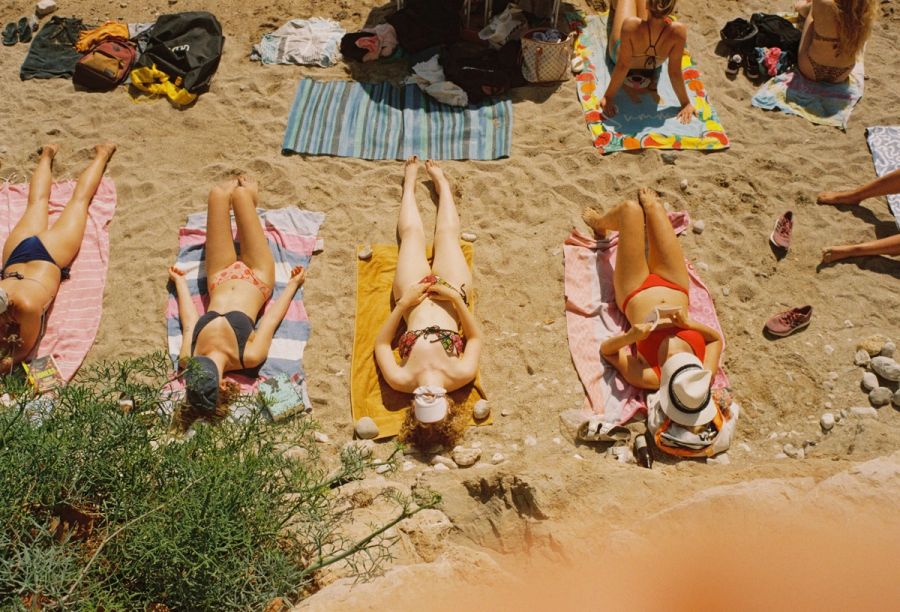 Four people sunbathing in a row on towels, seen from above. Film photograph by Nicolò Pudel