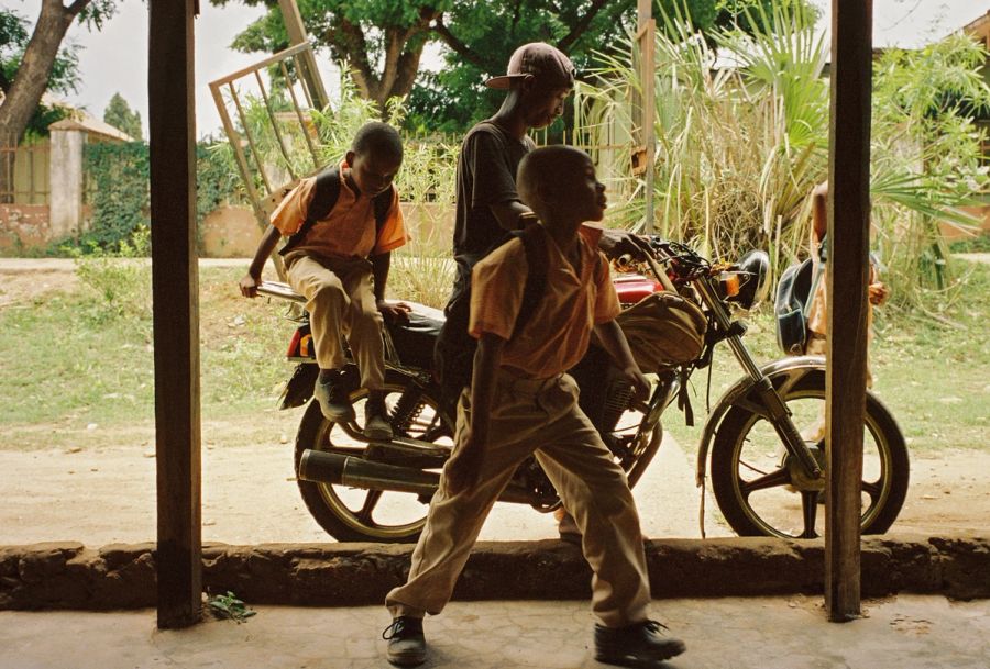 Schoolboys passing a parked motorbike in a doorway, Msambweni, Kenya. Film photograph by Nicolò Pudel
