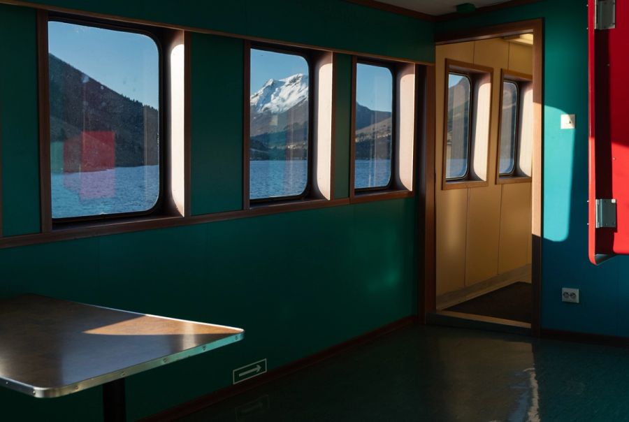 Green ferry cabin interior with snowy fjord mountains through the windows, Norway. Film photograph by Nicolò Pudel
