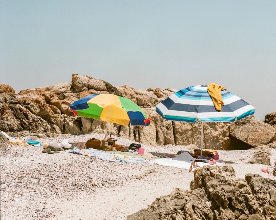 Two beach umbrellas among boulders on a stony shore, Cape Town. Film photograph by Nicolò Pudel