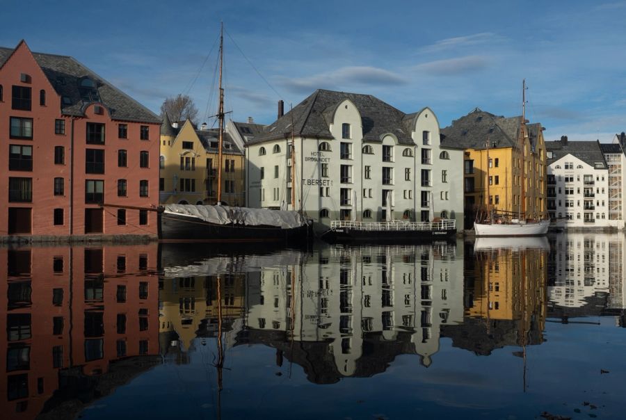 Pastel waterfront warehouses mirrored in still harbour water, Ålesund, Norway. Film photograph by Nicolò Pudel