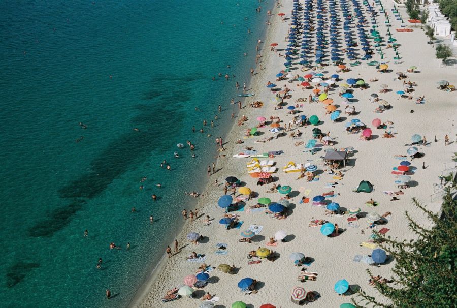 Crowded umbrella-filled beach and clear shallows seen from above, Italy. Film photograph by Nicolò Pudel