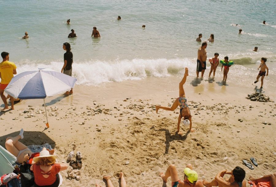 Child doing a handstand on a busy beach by the breaking waves, Cape Town. Film photograph by Nicolò Pudel