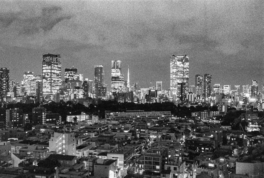 Tokyo skyline lit at night with lower residential buildings in foreground, film photograph by Nicolò Pudel.