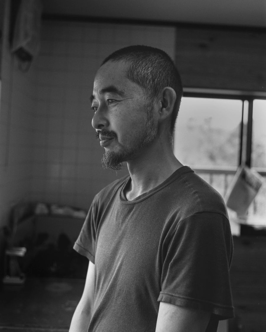A man in profile wearing a t-shirt gazes toward a window in an interior space, film photograph by Nicolò Pudel.